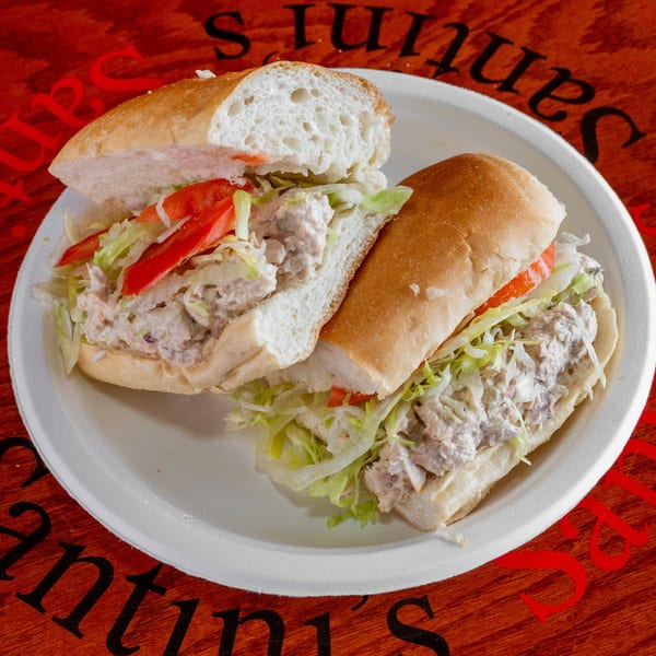 Two halves of a tuna sub sandwich with lettuce and tomato on a white plate.