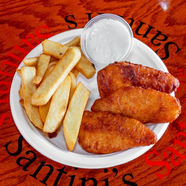 A plate of golden-brown fish and chips with a side of tartar sauce on a wooden table.