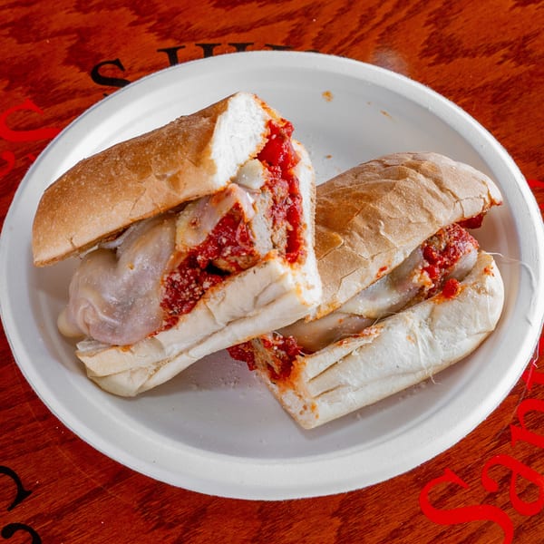Two meatball subs with marinara sauce, melted cheese, and onions served on a white plate atop a wooden table.