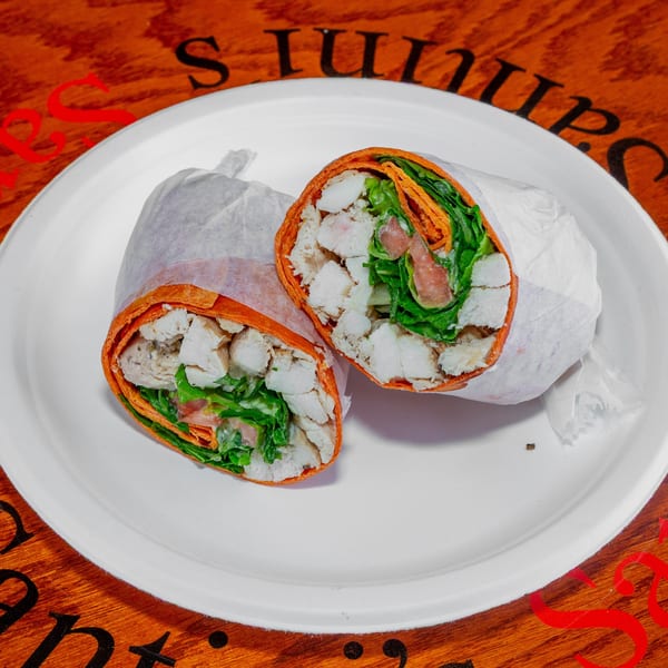 Two halves of a chicken and vegetable wrap on a white plate, on a wooden table.