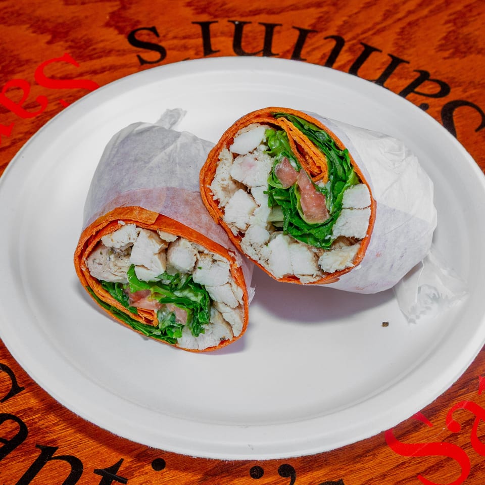 Two halves of a chicken and vegetable wrap on a white plate, on a wooden table.
