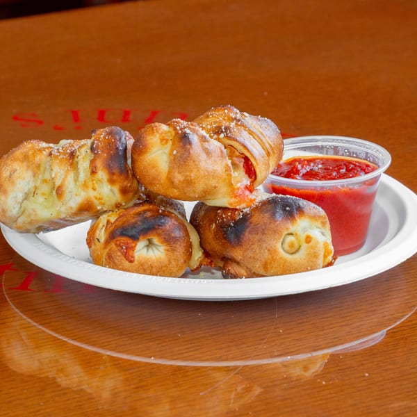 Four golden-brown pizza rolls with melted cheese and pepperoni, served with a side of marinara sauce.