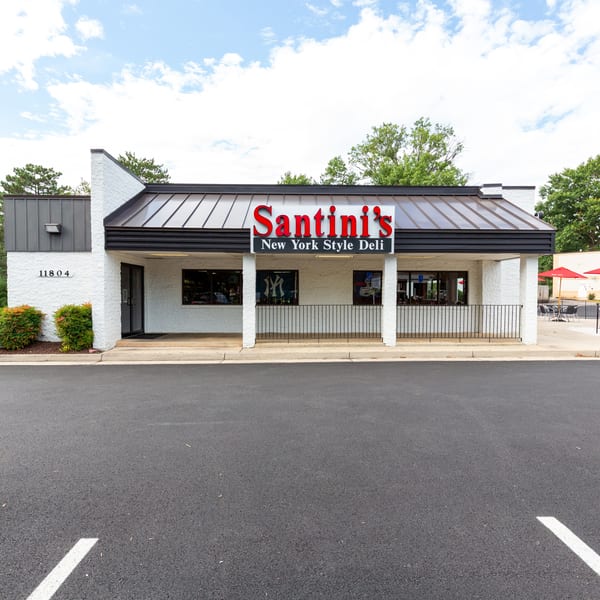 Exterior of Santini's New York Style Deli, a white building with a black roof and red umbrellas.