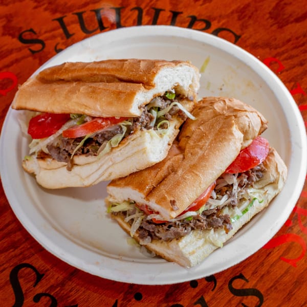 Two halves of a steak and cheese sub with lettuce, tomatoes, and onions on a white plate.