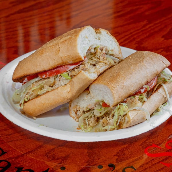 Two halves of a chicken sub sandwich with lettuce, tomato, and sauce on a white plate.