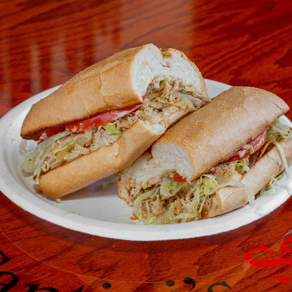 Two halves of a chicken sub sandwich with lettuce, tomato, and sauce on a white plate.