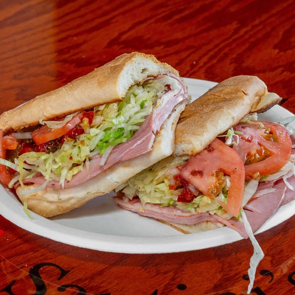 Two halves of a large deli sub sandwich with meat, cheese, lettuce, and tomatoes on a white plate.