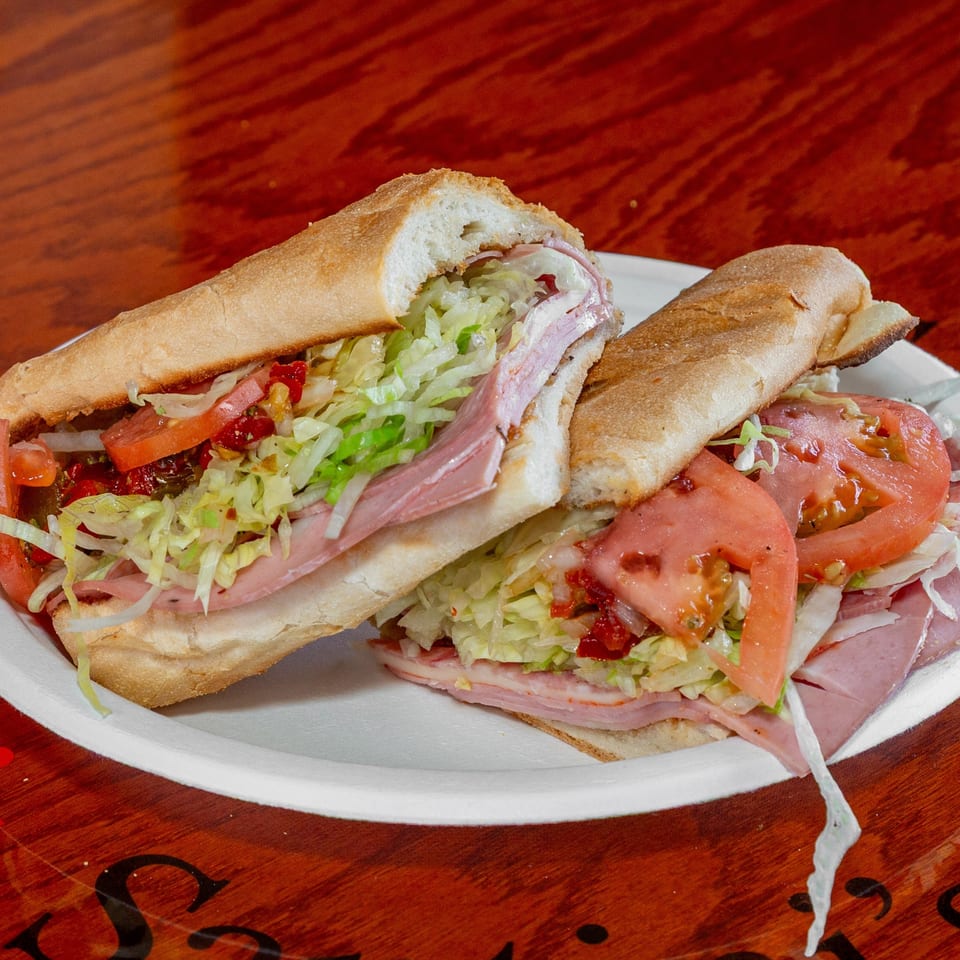 Two halves of a large deli sub sandwich with meat, cheese, lettuce, and tomatoes on a white plate.