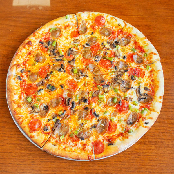 A whole pizza with pepperoni, sausage, mushrooms, and green peppers on a wooden table.