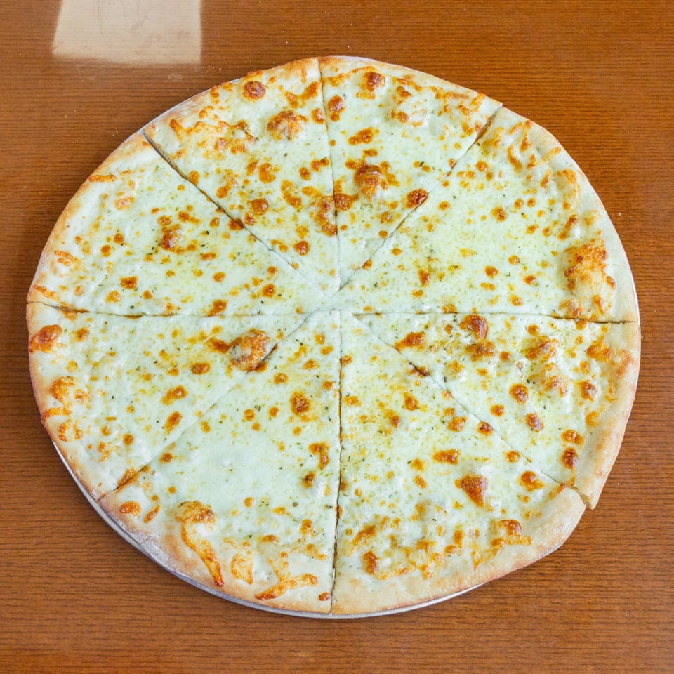 A whole white pizza with melted cheese and herbs, cut into eight slices on a wooden table.