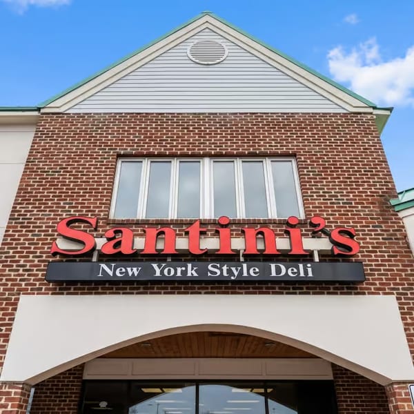 Santini's New York Style Deli sign on a brick building with white siding under a blue sky.