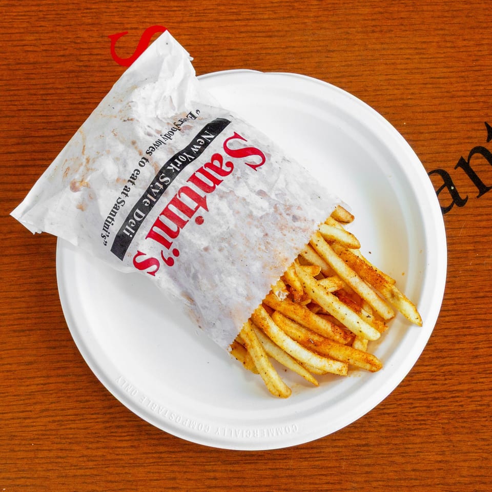 Santini's New York Style Deli seasoned fries in a paper bag on a white plate.